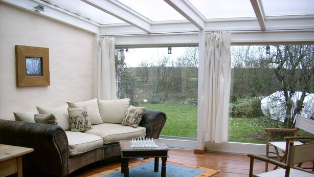 A conservatory with a wooden floor, a sofa with cushions, a chess table, and a chair. - Complete apartment with garden use (Nußloch)