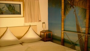 A bed with white linens and a wooden headboard, a nightstand with a lamp, a painting on the wall, and a mural of a palm tree and sky. - Complete apartment with garden use (Nußloch)