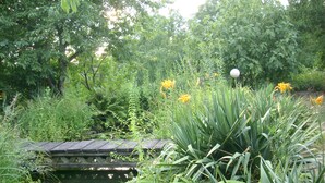 A wooden bridge over a pond surrounded by lush greenery and yellow flowers. - Complete apartment with garden use (Nußloch)