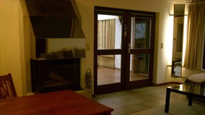 A living room with a wooden table and chairs, a fireplace, a sliding glass door leading to a balcony, and a small table with a lamp. - Complete apartment with garden use (Nußloch)