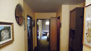 Un couloir étroit, avec un tableau encadré sur le mur de gauche, un miroir et une porte donnant sur une autre pièce.