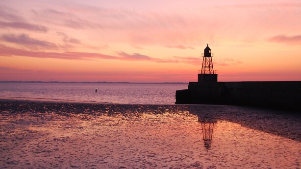 Un phare au coucher du soleil, avec une plage au premier plan.