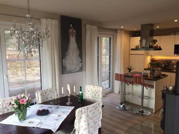 A dining area with a table set for two, a chandelier, and a large window with curtains.