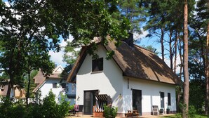 Un bâtiment blanc avec un toit de chaume, entouré d’arbres et d’une pelouse où se trouve une table de pique-nique.