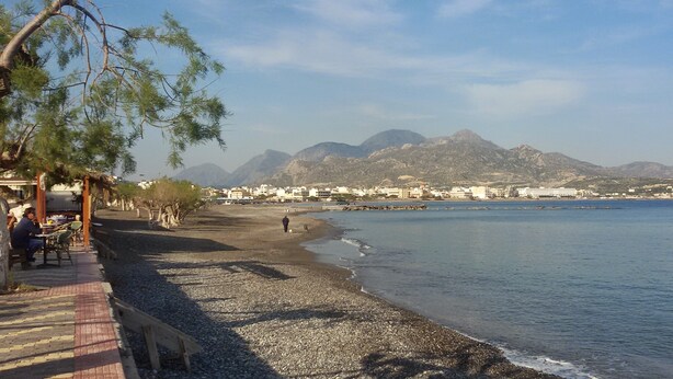 A beach with pebbles, a wooden walkway, and a view of mountains in the distance. - In the narrow streets of the old town, family-friendly, close to the beach (Ierapetra)