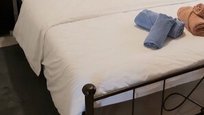 A neatly made double bed with white linens, a black metal headboard, and a small bedside table with a lamp. - In the narrow streets of the old town, family-friendly, close to the beach (Ierapetra)