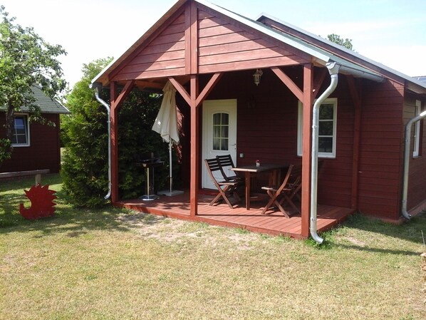 Une petite cabane en bois rouge, dotée d’une véranda, d’une table et de deux chaises.