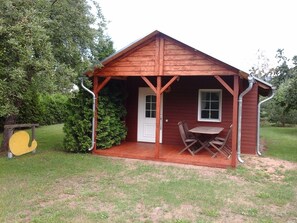 Une petite cabane en bois avec une véranda, une porte et une table entourée de chaises.