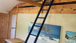 A room with a wooden ceiling, a blue ladder, a grey sofa, and two paintings on the wall. - 6 cottages ideal for family gatherings near the Spreewald. (Lübbenau/Spreewald)