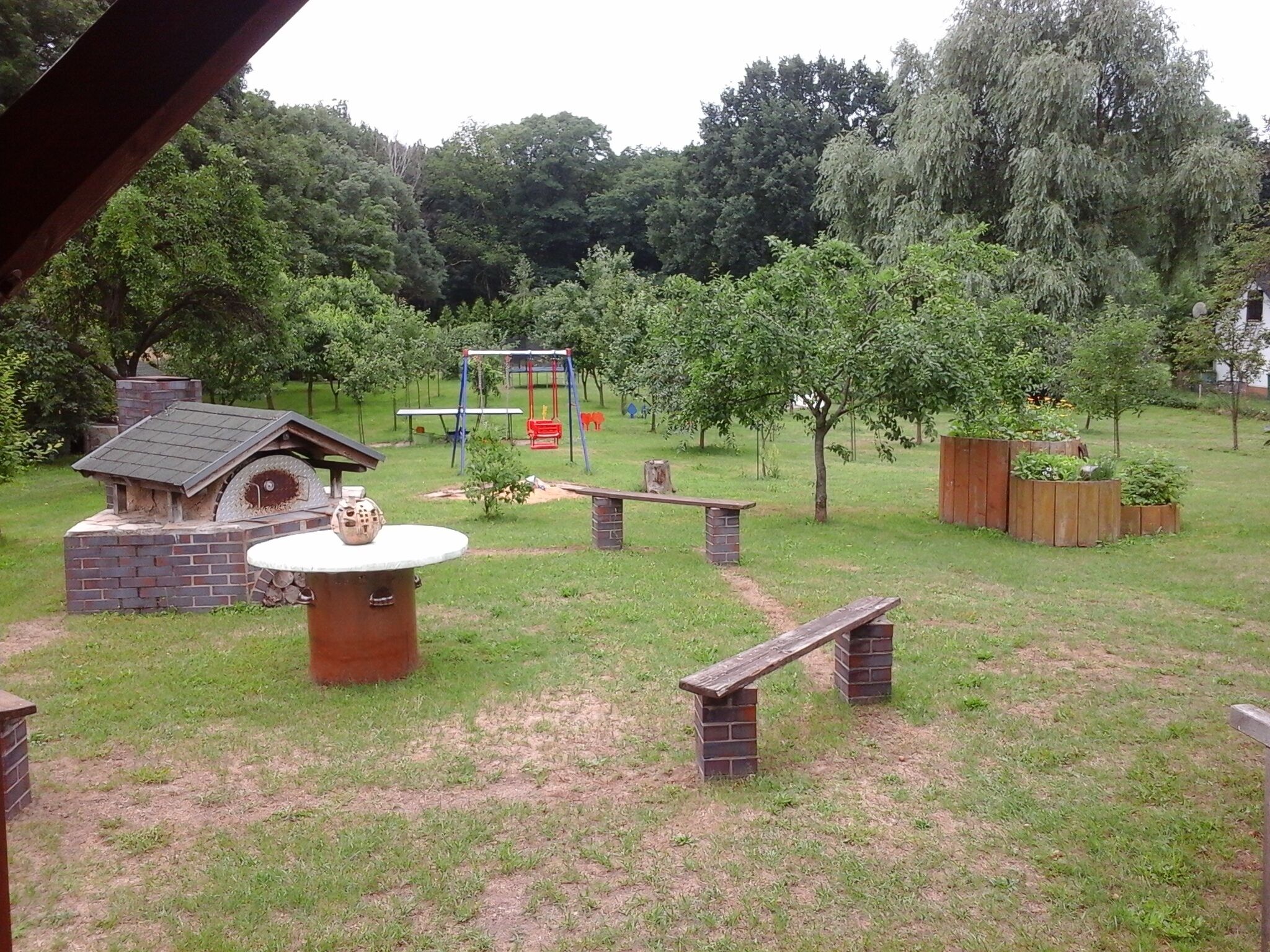 Un giardino sul retro con un'area barbecue in mattoni, un'altalena e una panchina in legno.
