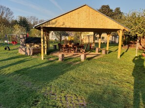 Un pavillon en bois, doté d’une base en briques, entouré d’une pelouse où se trouvent une table de pique-nique et des chaises.