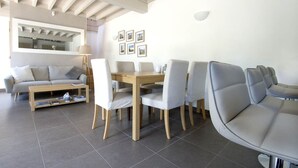 A modern living room with a dining area, featuring a wooden dining table, white upholstered chairs, a sofa, and a large mirror. - L'OEUILLADE: calm and tranquility in Champagne (Œuilly)