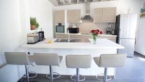 A modern kitchen with a central island, bar stools, built-in appliances, and a pendant light. - L'OEUILLADE: calm and tranquility in Champagne (Œuilly)