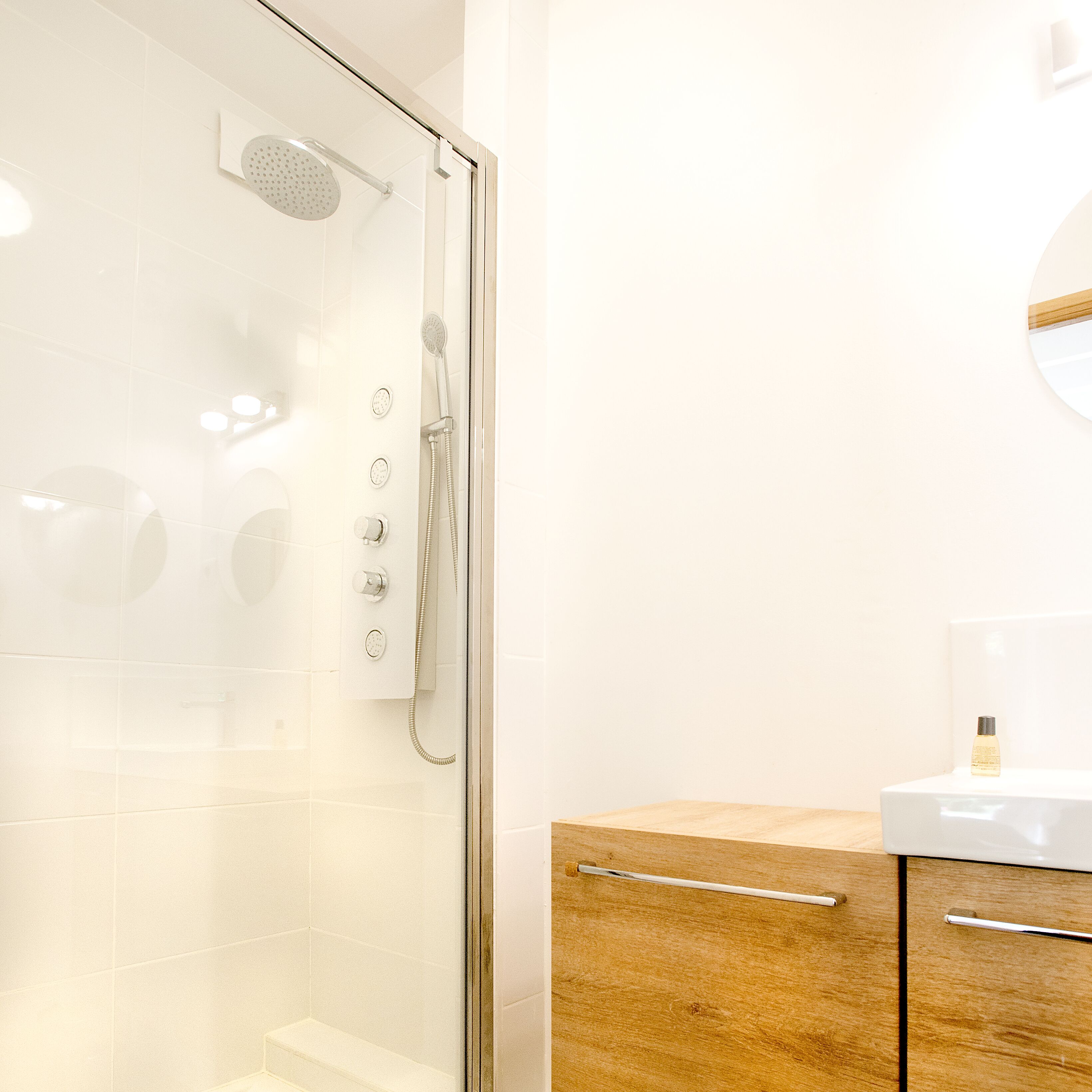 Ein modernes Badezimmer mit einer Glasdusche, einem Holzkästen und einem weißen Waschbecken.