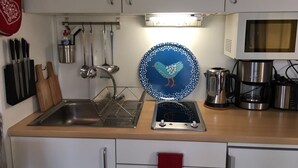 Una cucina compatta con lavello, fornello e forno a microonde. Utensili pensili sopra il lavello e un bollitore sul bancone.
