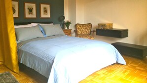 Una camera da letto con un letto, una sedia, un comodino, una mensola e quadri appesi al muro.