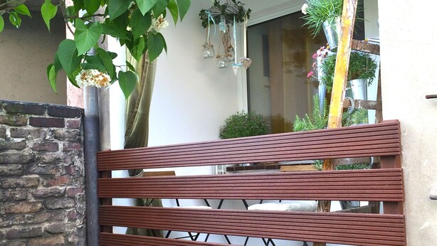 Una panchina di legno in un'area esterna con un muro in mattoni e una pianta pensile.