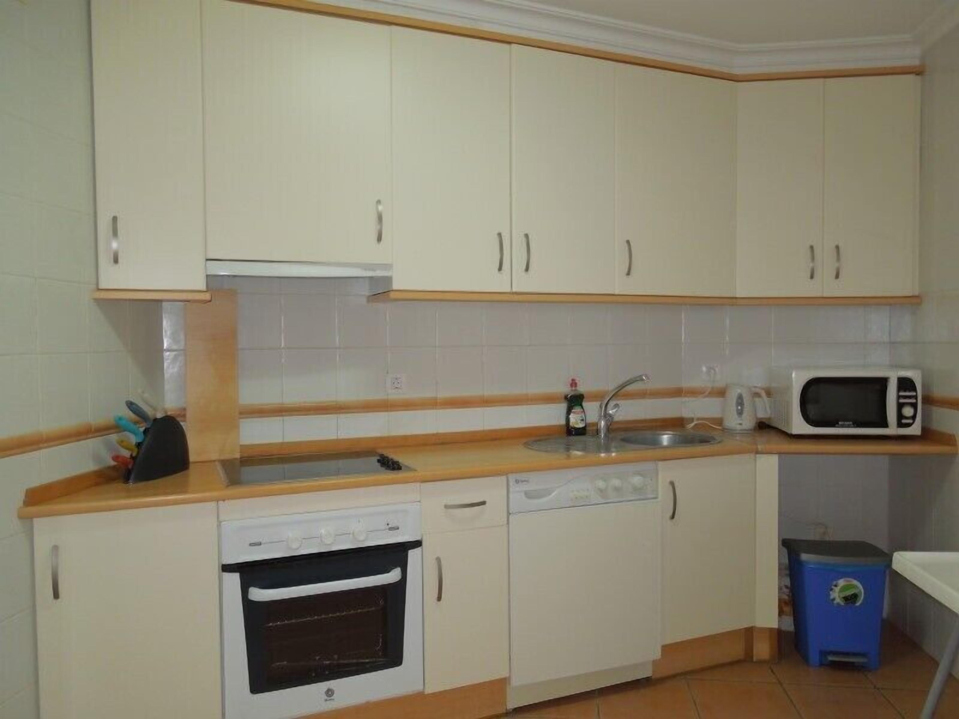 A compact kitchen with white cabinets, a dishwasher, an oven, a microwave, and a sink.