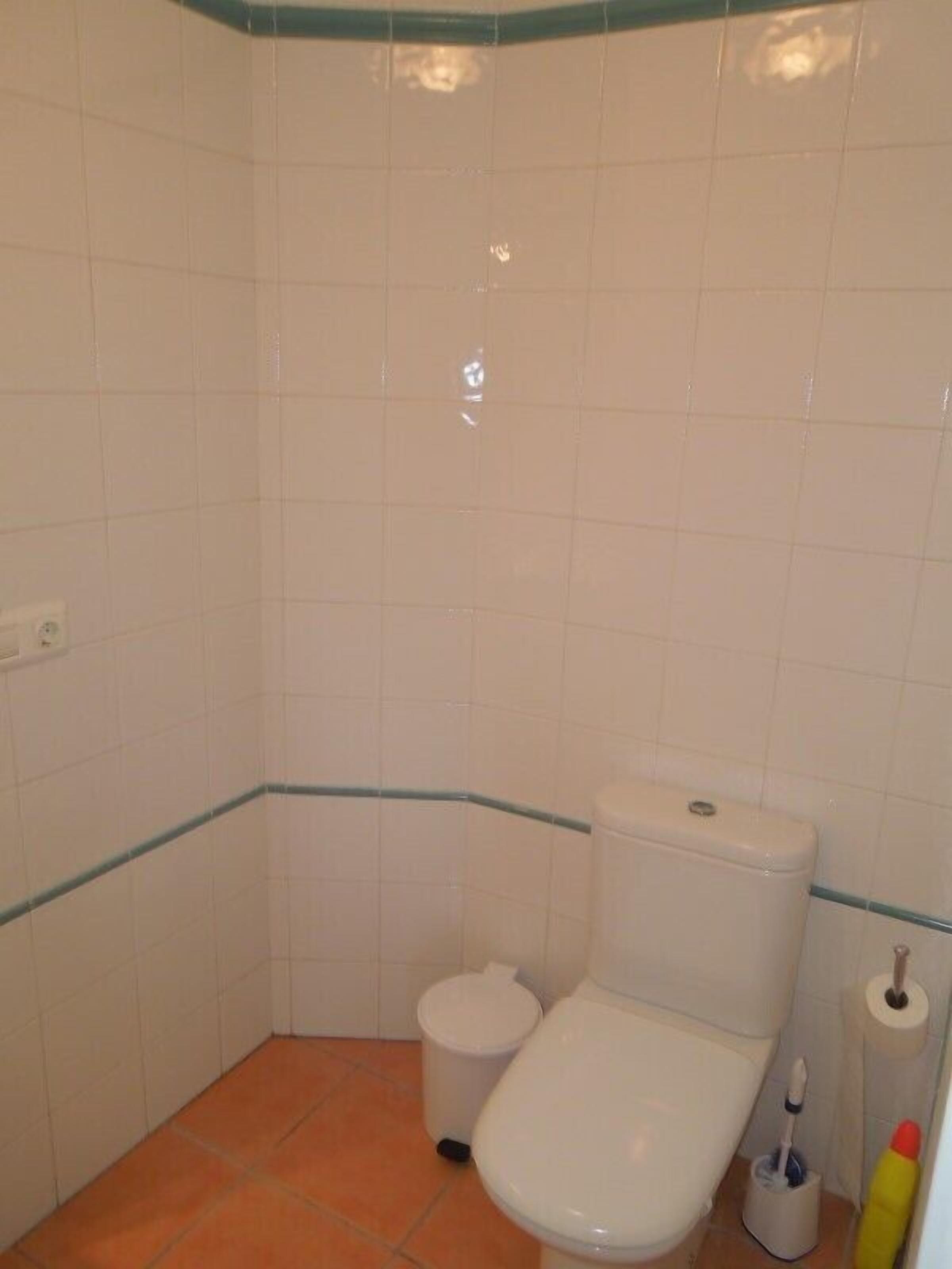 Ein kleines Badezimmer mit Fliesen, einer Toilette, einem Mülleimer und einem Toilettenpapierhalter.
