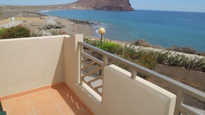En balkon med udsigt over en strand, klippelandskab og et bjerg i det fjerne.
