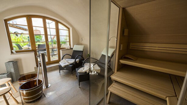 A spa room with a sauna, two chairs, a wooden bench, and a large window with a view of greenery.