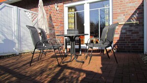 A patio with a brick floor, a table, and four chairs. - Comfortable holiday home **** (incl. W-Lan) in the best location of Carolinensiel (Carolinensiel)