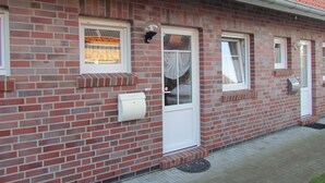 A brick building with a red-tiled roof, white-framed windows, and a door with a glass panel. - Comfortable holiday home **** (incl. W-Lan) in the best location of Carolinensiel (Carolinensiel)