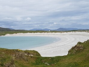 A coastal landscape with a sandy beach, a clear blue sea, and distant mountains under a cloudy sky. - House between coast, lake + mountains: every window view is a Connemara highlight! (Roundstone)