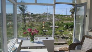 A conservatory with a glass door, white tables, a wicker chair, and a vase with pink flowers.