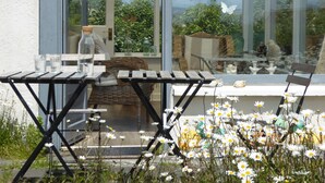 A patio with a table and chairs, a wicker chair, and a glass table with a bottle and glasses.