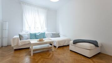 Un salon minimaliste avec un ensemble de canapés, une table basse et une fenêtre ornée de rideaux légers.