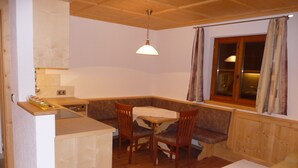 A cozy room with a wooden ceiling, a dining table with chairs, a window with curtains, and a small kitchenette area.