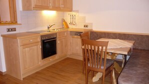 A compact kitchen with wooden cabinets, a built-in oven, a sink, and a dining area with a bench and table.
