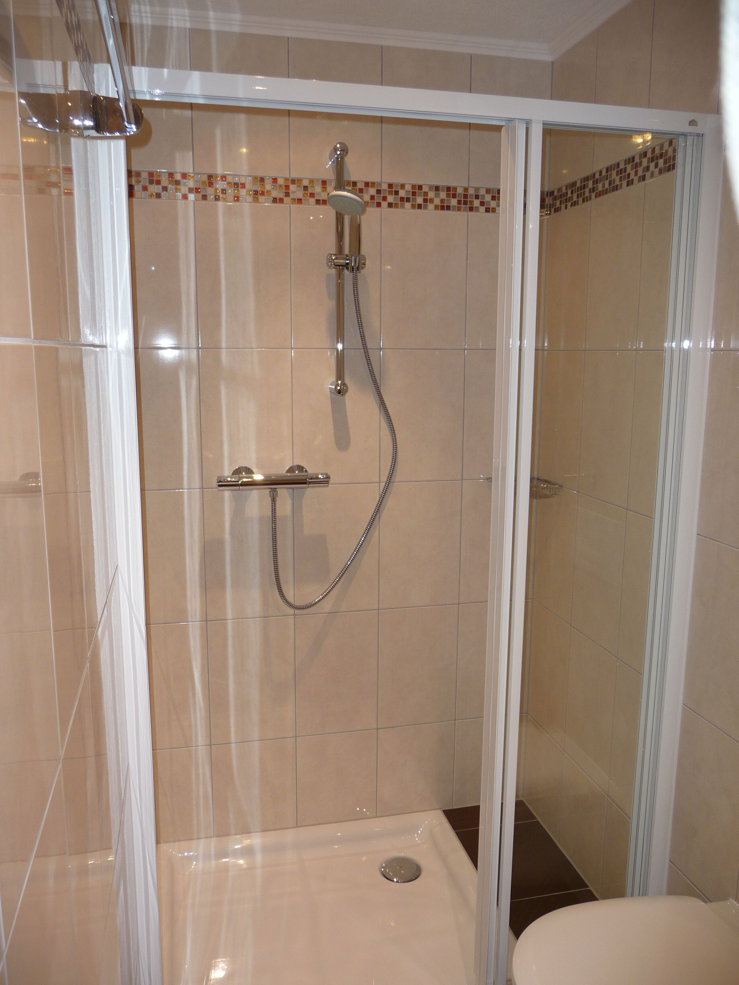 A walk-in shower with a glass door, tiled walls, and a showerhead with a handheld attachment.