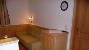 A small room with a wooden floor, a beige sofa, a wooden cabinet, a clock on the wall, and a door.