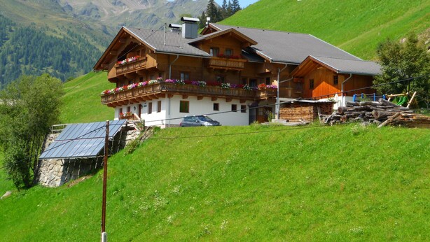 A traditional wooden chalet with balconies, a stone foundation, and a view of mountains.