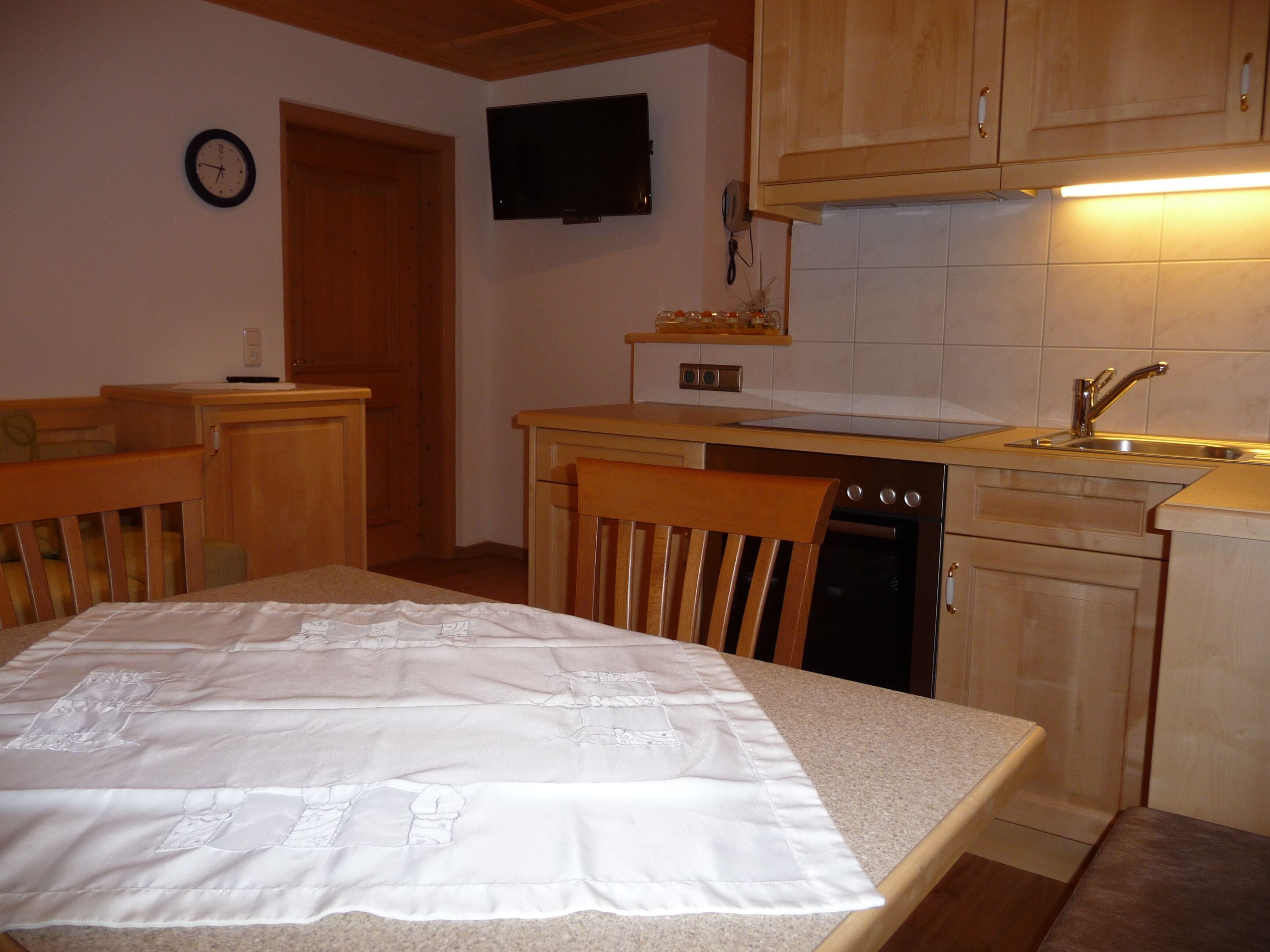 A compact kitchen with wooden cabinets, a built-in oven, a sink, and a television mounted above the counter.