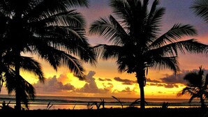 Een strandzicht met silhouetten van palmbomen voor een zonsonderganglucht.