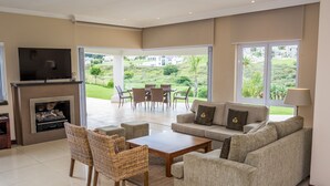 A living room with a sofa, chairs, a coffee table, a fireplace, and a TV. - Modern house, solar-heated pool & stunning views, at Kingswood Golf Resort (George)