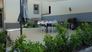 En udendørs terrasse med et bord, stole, planter og en grill.