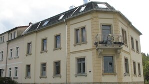 En hjørnebygning med mange vinduer, en balkon med gelænder og en stensokkel.