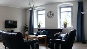 En stue med en lædersofa, et træbord, et fladskærms-tv og et vægur.