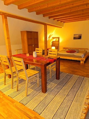 A wooden dining table with chairs, a rug, a bed with pillows, and a lamp.