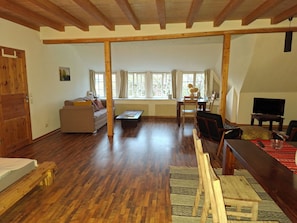 A spacious living area with a wooden floor, a sofa, a dining table, and a television.