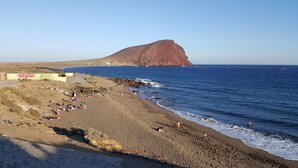 A beach with a rocky outcrop in the background, a sign with 'RECK' and 'SUGE' on the left, and a clear blue sky. - Casa Soleada close to sea + beach, 2 pools, terrace, sea views,TV, Wifi (Granadilla)