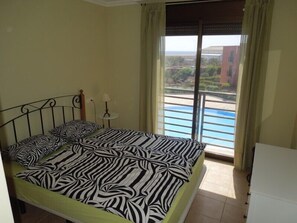 Un dormitorio con una cama, una mesita de noche, una lámpara y vista a una piscina a través de una puerta corrediza.