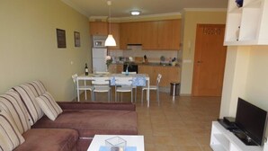 A living room with a brown sofa, a white coffee table, and a TV stand. There is a dining area with a table and chairs, and a kitchen in the background. - Casa Soleada close to sea + beach, 2 pools, terrace, sea views,TV, Wifi (Granadilla)