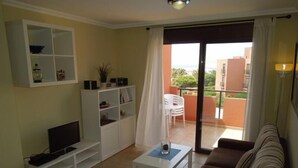 A living room with a sofa, TV, white shelving unit, and a balcony with a table and chairs. - Casa Soleada close to sea + beach, 2 pools, terrace, sea views,TV, Wifi (Granadilla)