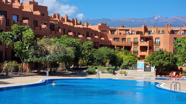 A swimming pool surrounded by a building with a mountainous backdrop. - Casa Soleada close to sea + beach, 2 pools, terrace, sea views,TV, Wifi (Granadilla)