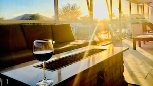 A modern interior with a glass table, a glass of red wine, and a view of the outdoors.